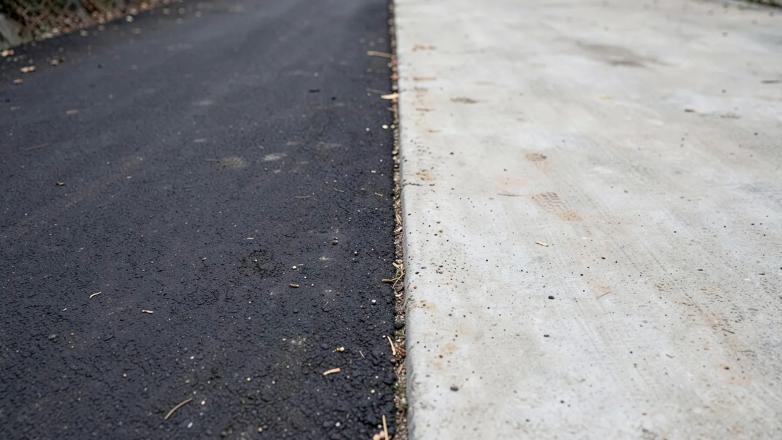 Dark asphalt and pale broom-finished concrete meeting along a straight seam, shown side by side under the same light.